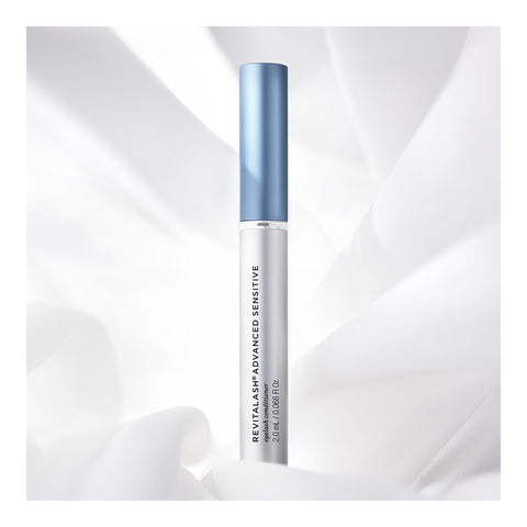 A slender RevitaLash Advanced Eyelash Conditioner and Enhancing Serum Sensitive (2.0mL 3 Mo.Supply) tube with a pale blue cap and sleek silver body against white fabric, infused with peptides and botanicals for gentle care.