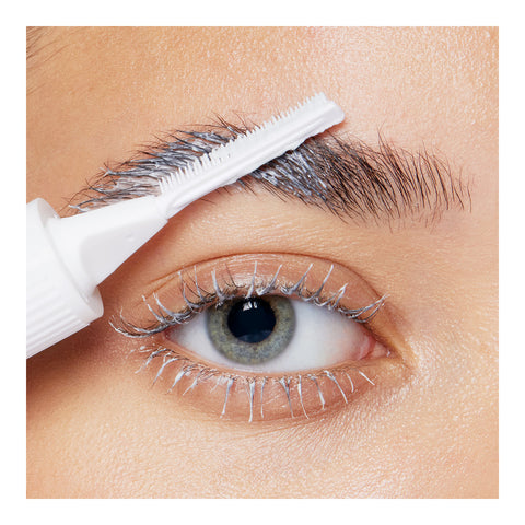 A close-up of a persons eye shows mascara creating a frosty effect, while a white applicator brushes the eyebrow with RevitaLashs Lash and Brow Masque for a glossy look, and the skin appears smooth thanks to nutrient-rich ingredients.