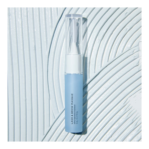 A sleek blue RevitaLash Lash and Brow Masque tube with nutrient-rich ingredients sits on a textured white surface with curved patterns. Its transparent cap complements the black text, promoting revitalization of compromised lashes and brows.