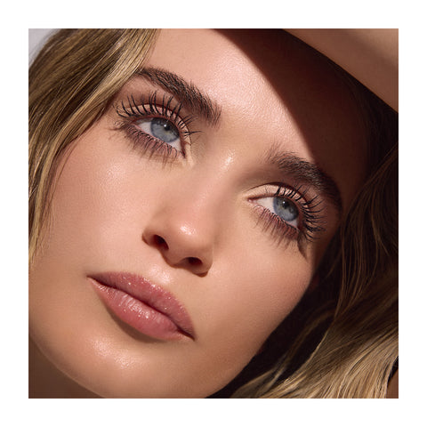 A close-up captures blue eyes gazing upward with long lashes enhanced by RevitaLash Length Define Tubing Mascara 5mL. Their smooth skin and natural makeup highlight their features, while blonde hair frames their face and a shadow partially covers their forehead.