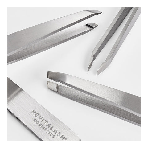 Four professional-grade slanted and pointed tweezers gleam in silver on a white surface. One, engraved with RevitaLash on its handle, embodies the brands dedication to precision, quality, and care.